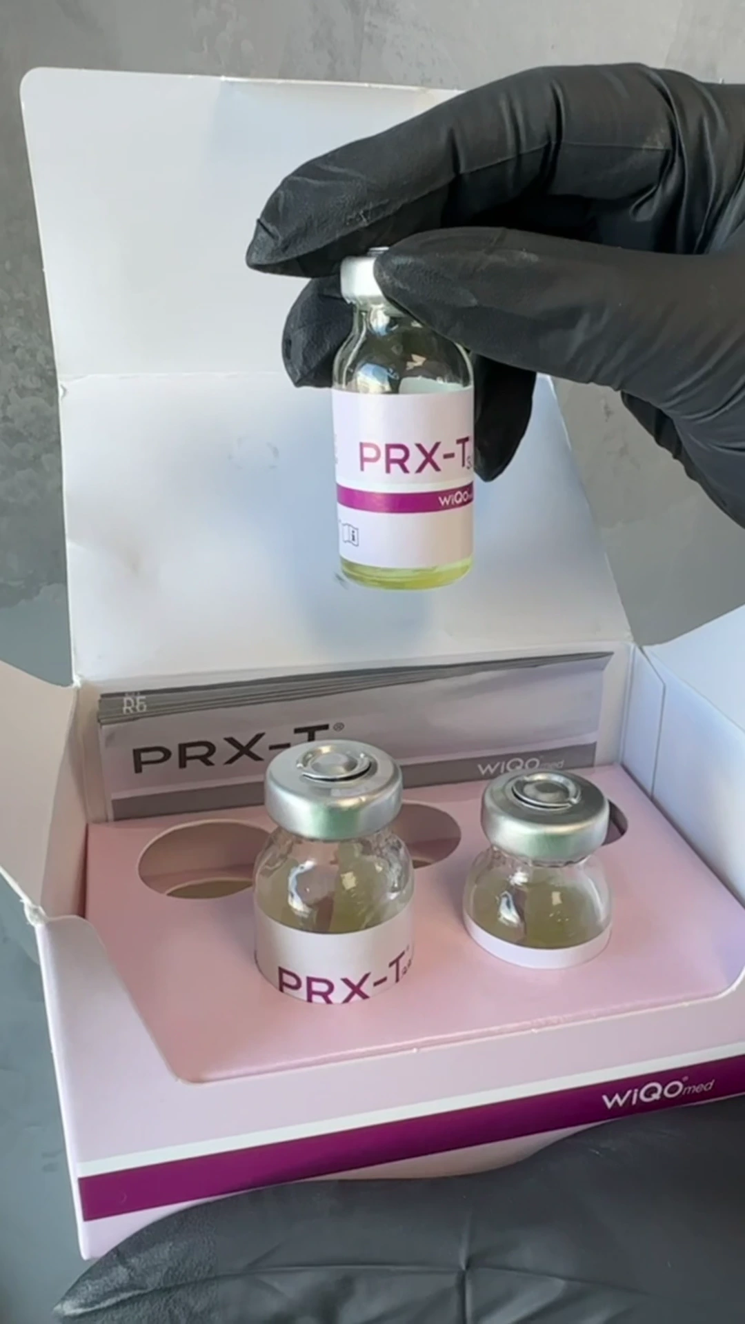 A gloved hand holding a PRX-T33 vial above its open box.