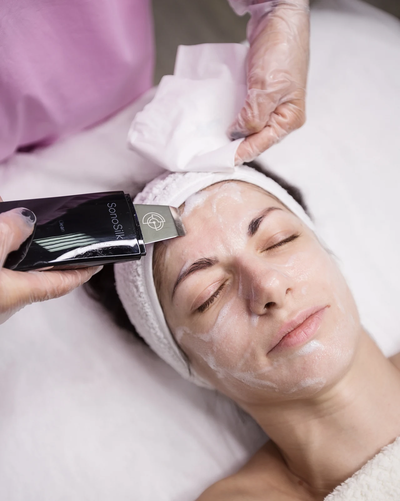 Hands using a facial spatula on a client's forehead during a facial treatment.