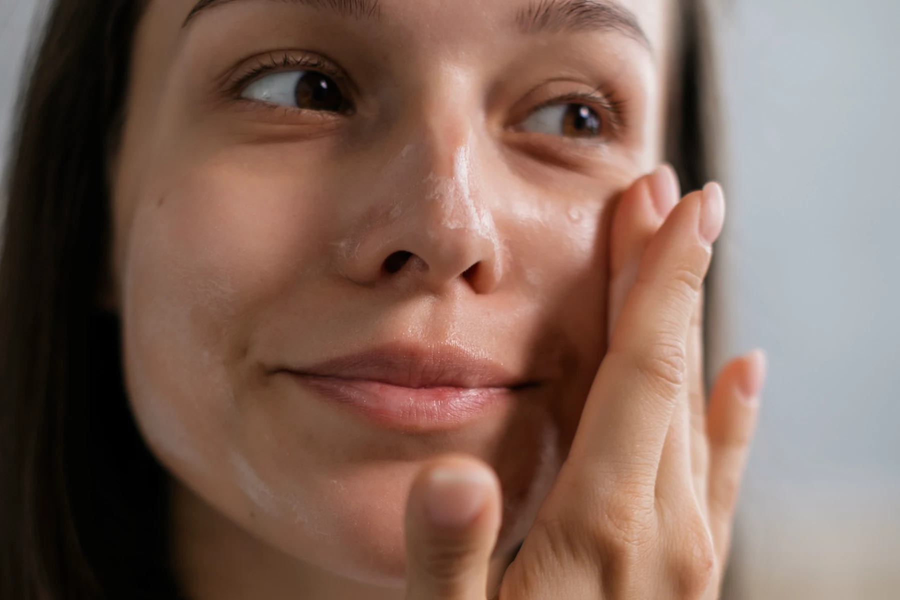 A woman gently applying skin care cream to her cheek.