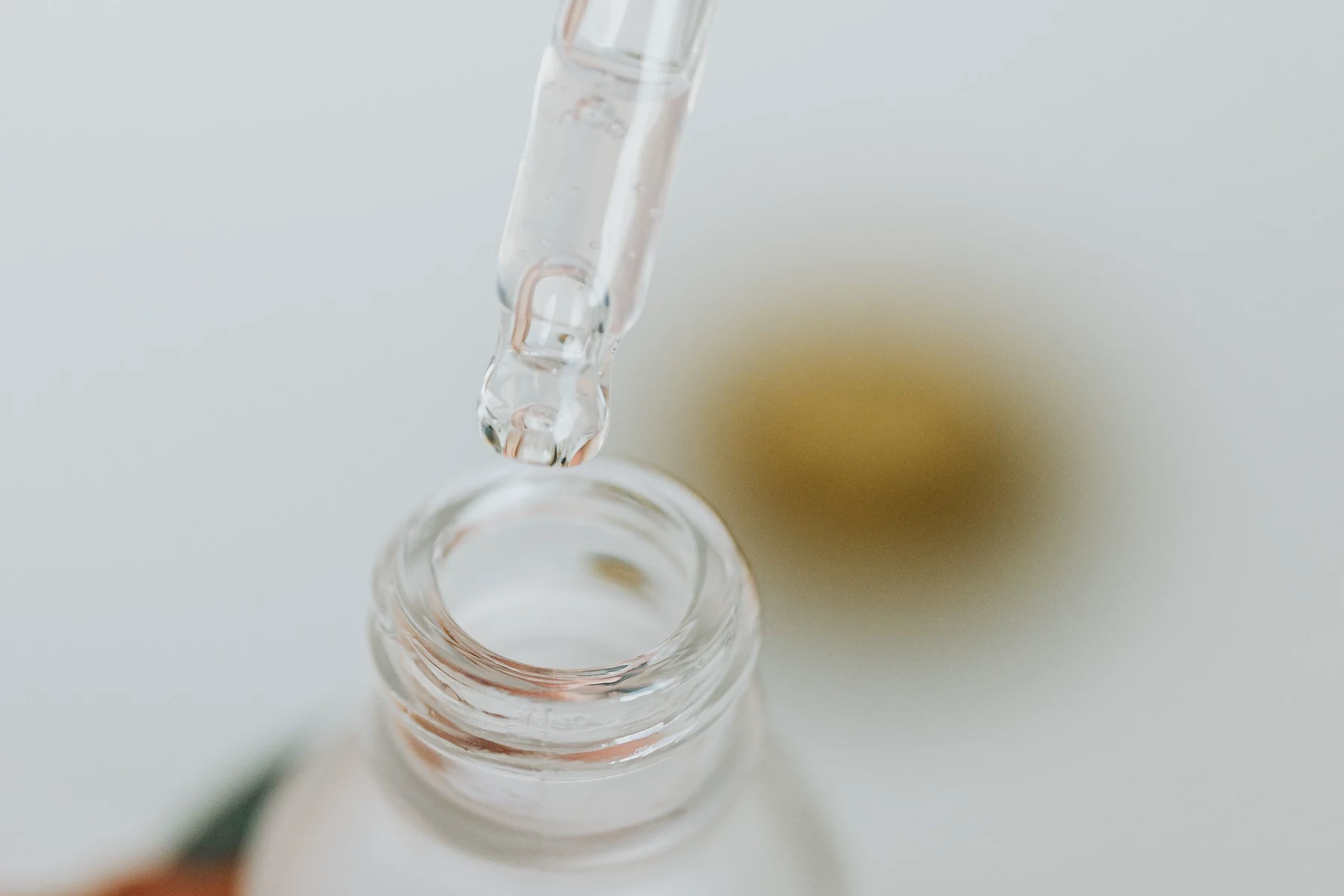 A glass dropper held above an unlabelled skin care bottle.